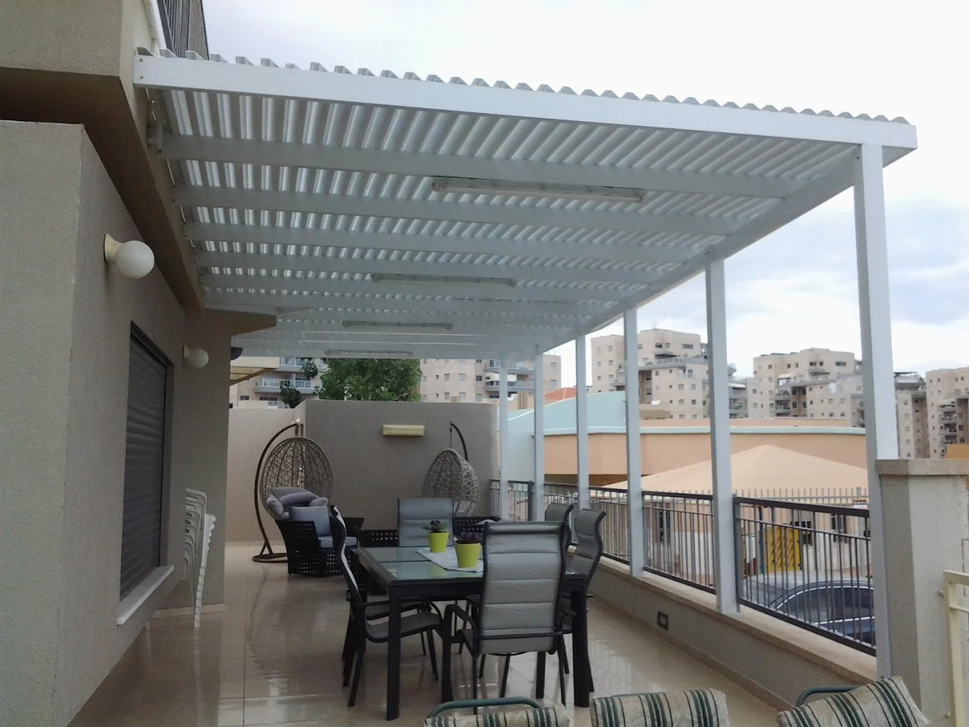 פרגולת אלומיניום בהירה על עמודים במרפסת שמש של דירה עם פינת ישיבה