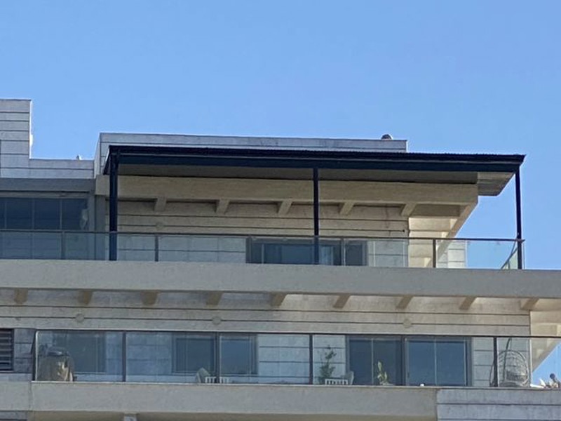 פרגולת אלומיניום צמודת קיר במרפסת גג של בניין מגורים